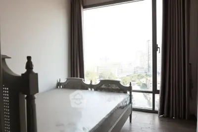 Bright bedroom with large window offering city view and elegant bed frame.