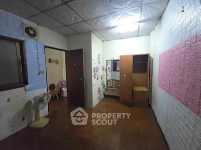 Cozy bedroom with wooden flooring and decorative walls, featuring a wardrobe and fan.