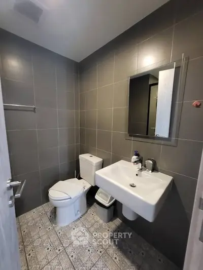Modern bathroom with sleek fixtures and tiled walls, featuring a toilet, sink, and mirror.
