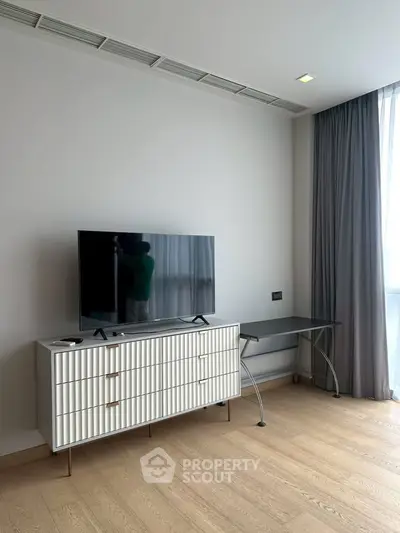 Modern living room with sleek TV stand and large window, offering ample natural light and minimalist design.