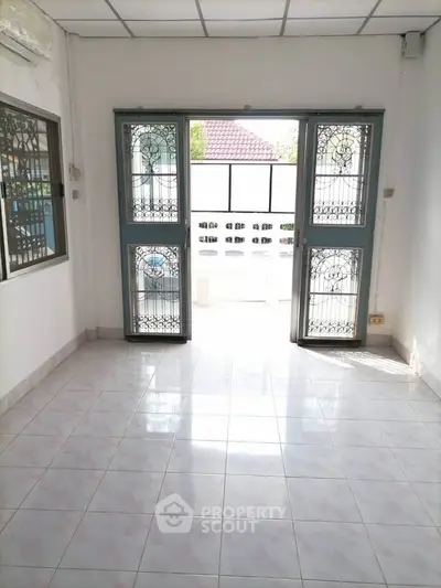 Bright empty room with tiled floor and decorative metal doors leading to outdoor area.