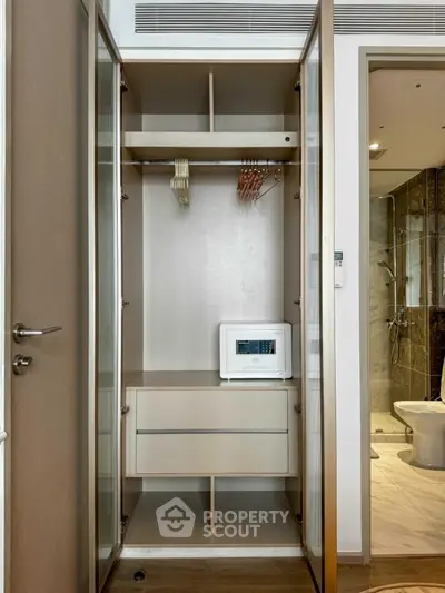 Modern apartment closet with built-in safe and hangers, adjacent to a stylish bathroom.