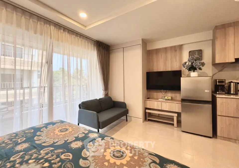 Modern studio apartment with cozy living area and kitchenette, featuring a stylish sofa and large window for natural light.