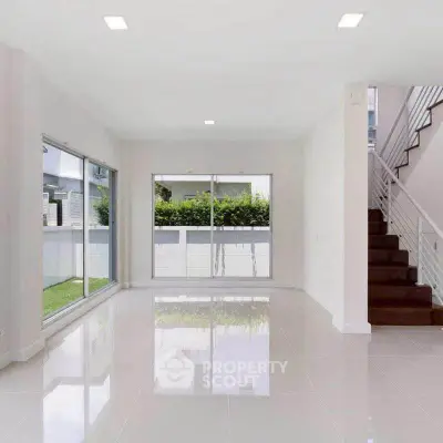 Spacious modern living room with large windows and garden view, featuring sleek tile flooring and staircase.