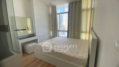 Modern bedroom with large window and city view, featuring a comfortable bed and sleek furniture.