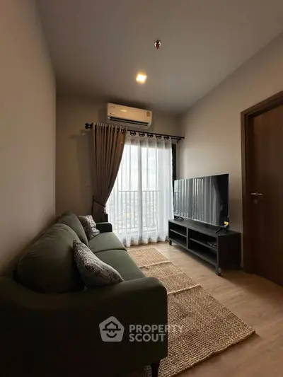 Cozy living room with modern decor, featuring a plush sofa, large TV, and natural light from a balcony window.