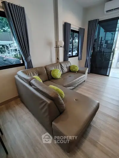 Modern living room with stylish gray sofa and large windows offering natural light and outdoor view.
