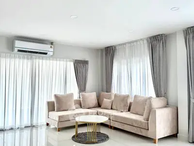 Elegant living room with plush beige sofa and modern decor, featuring large windows and ample natural light.