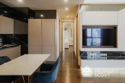 Modern kitchen with sleek black countertops, integrated appliances, and a spacious dining area leading to a well-lit hallway.