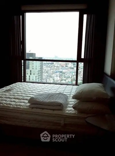 Cozy bedroom with large window offering stunning city view, perfect for urban living.