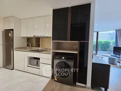 Modern kitchen with sleek appliances and open layout, featuring a washing machine and spacious living area view.