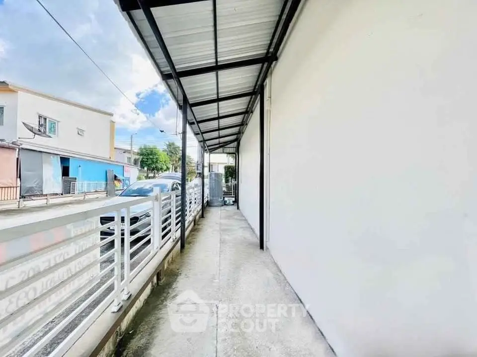 Modern exterior walkway with metal roof and white walls in urban residential area.