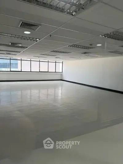 Spacious and well-lit commercial office space with reflective flooring, drop ceiling, and ample natural light from large windows, ideal for a corporate setup.