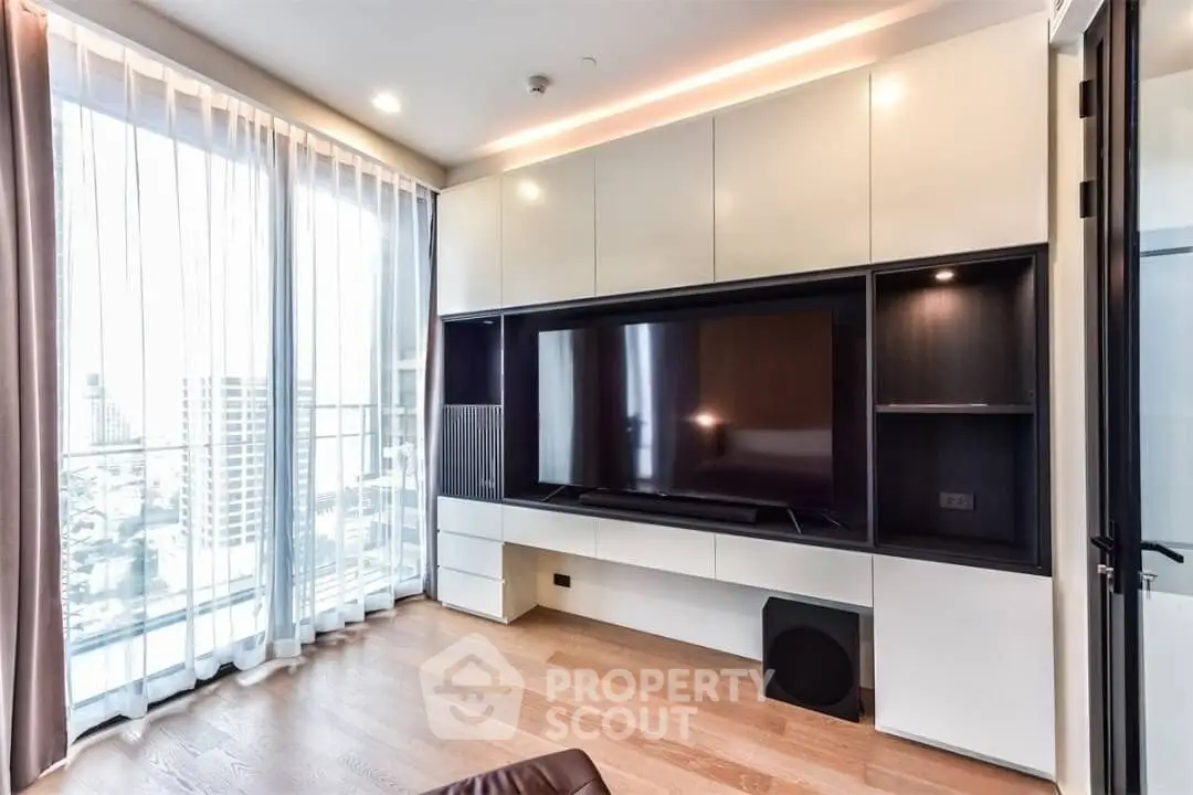 Modern living room with large TV, floor-to-ceiling windows, and sleek cabinetry in a high-rise apartment.
