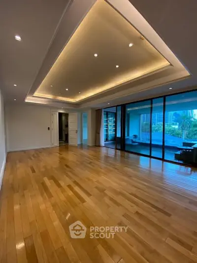 Spacious modern living room with wooden flooring and large glass doors opening to a balcony.