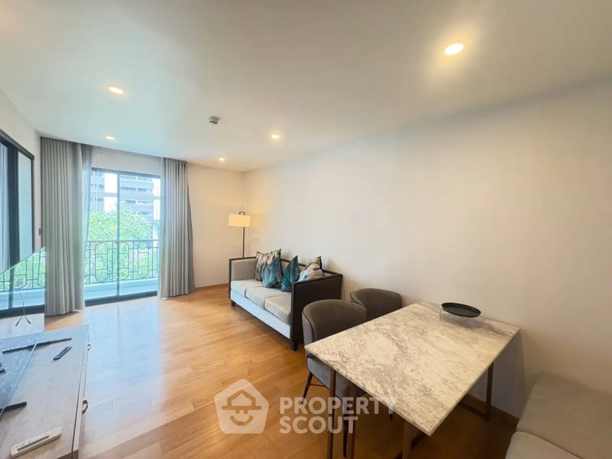 Spacious living room with modern decor and large windows offering natural light and a view of greenery.