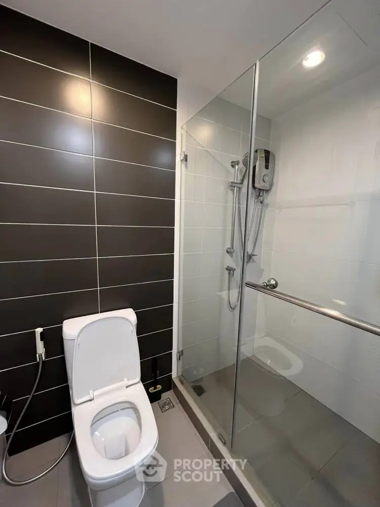 Modern bathroom with sleek glass shower and stylish dark tile wall.
