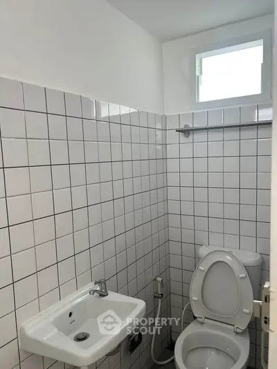 Compact bathroom with white tiled walls and small window.