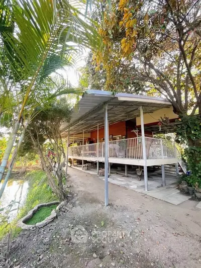 Charming elevated house with spacious porch surrounded by lush greenery and serene pond view.