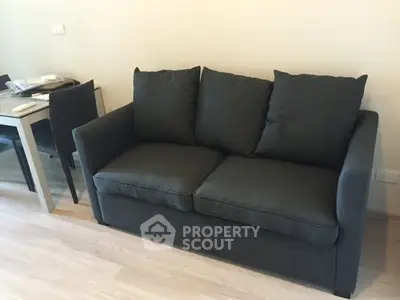 Modern living room with stylish dark sofa and dining table set on wooden flooring.