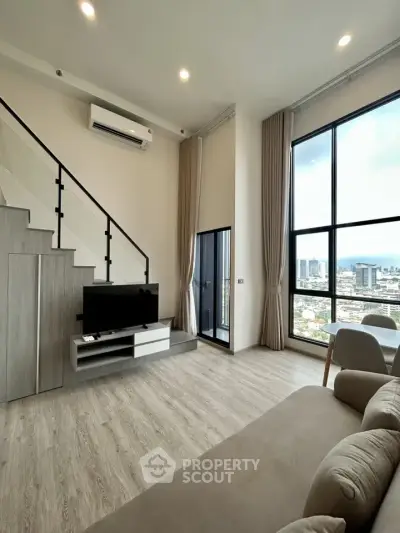 Modern living room with high ceilings and city view, featuring a staircase and sleek furnishings.