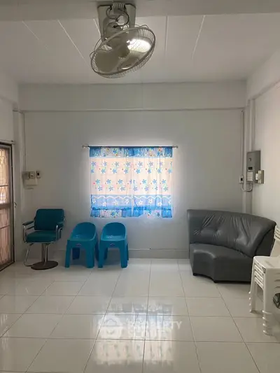 Spacious living room with tiled floor and simple furniture, featuring a ceiling fan and natural light.