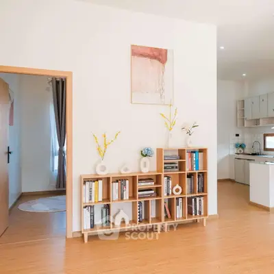 Modern open-plan living area with stylish bookshelf and kitchen view.
