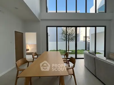 Modern living room with high ceilings and large windows overlooking a private garden, featuring sleek furniture.