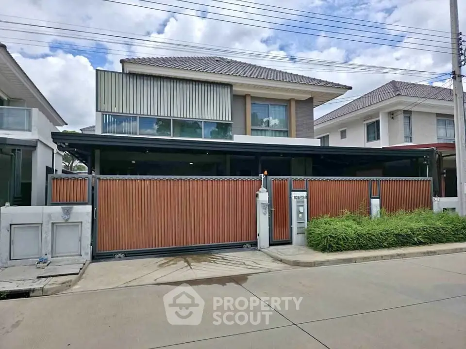 Modern two-story house with sleek design and gated entrance in a suburban neighborhood.