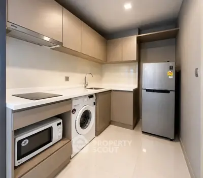 Modern kitchen with sleek cabinetry, washing machine, and stainless steel fridge in a compact layout.