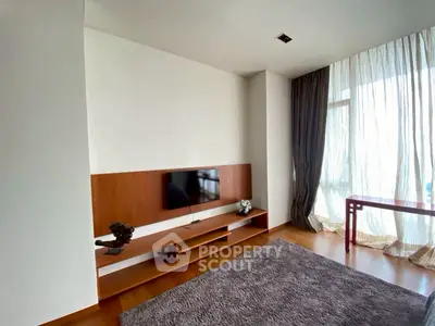 Modern living room with sleek wooden TV stand and large window with sheer curtains.
