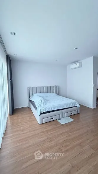 Spacious bedroom with modern decor and natural light, featuring a comfortable bed and sleek wooden flooring.