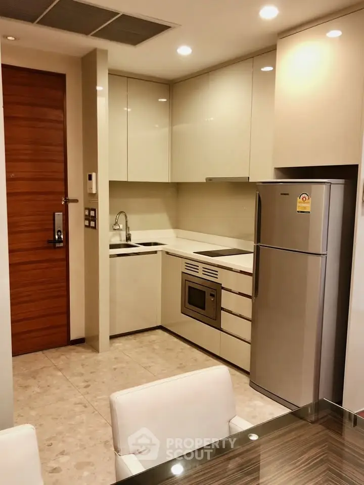 Modern kitchen with sleek cabinets, stainless steel fridge, and built-in oven in a compact layout.