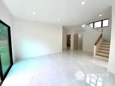 Spacious and bright living room with polished marble floors, large windows, and an elegant staircase leading to the upper level, perfect for luxurious living.