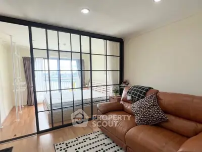 Modern living room with leather sofa and glass partition leading to a bright bedroom with a view.