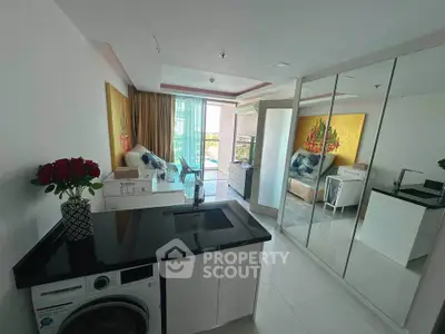Modern open-plan living room with mirrored wardrobe and washing machine, featuring vibrant artwork and balcony view.