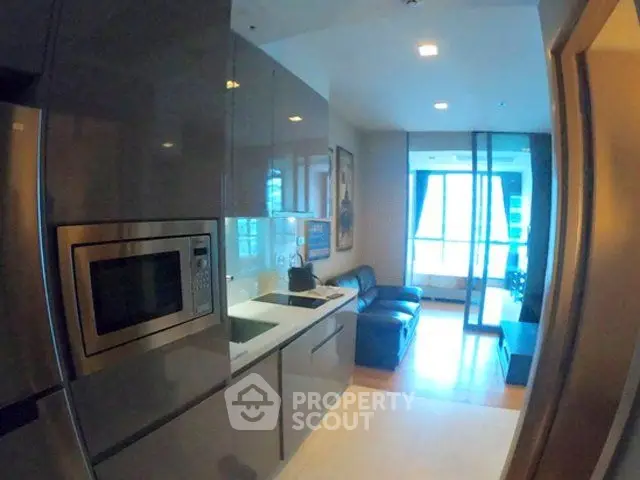 Modern kitchen with sleek cabinetry and cozy living area in open layout apartment.