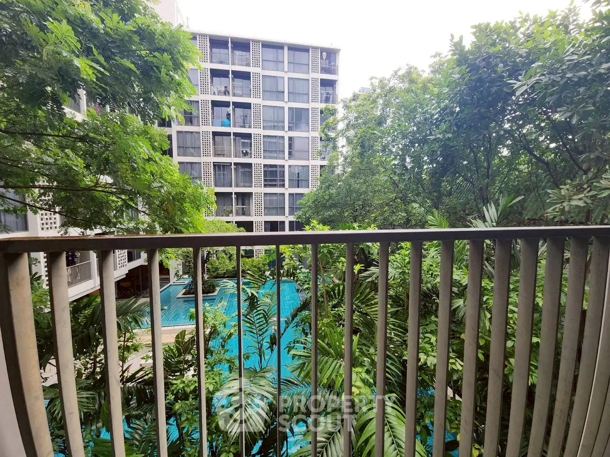 Stunning view from balcony overlooking lush garden and pool in modern apartment complex.