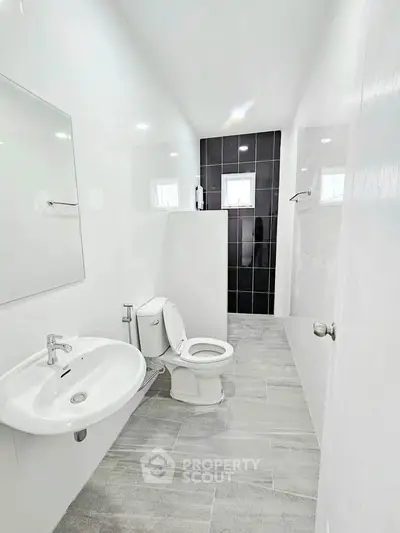 Modern bathroom with sleek design, featuring a white sink, toilet, and stylish black-tiled shower area.