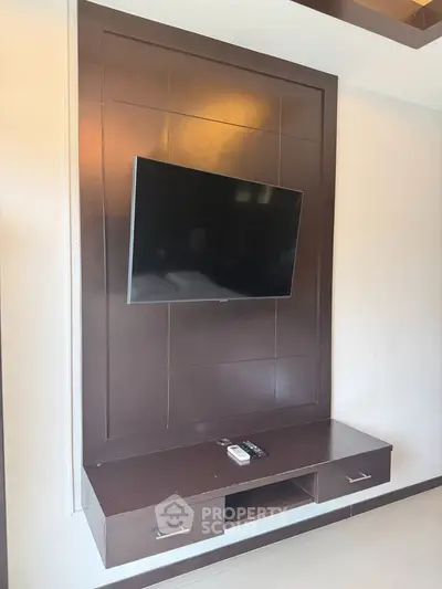 Modern living room with wall-mounted TV and sleek wooden entertainment unit.