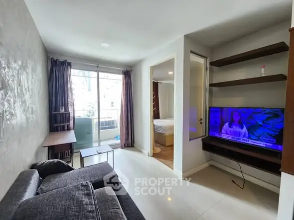 Modern living room with balcony access and TV, featuring sleek furniture and natural light.