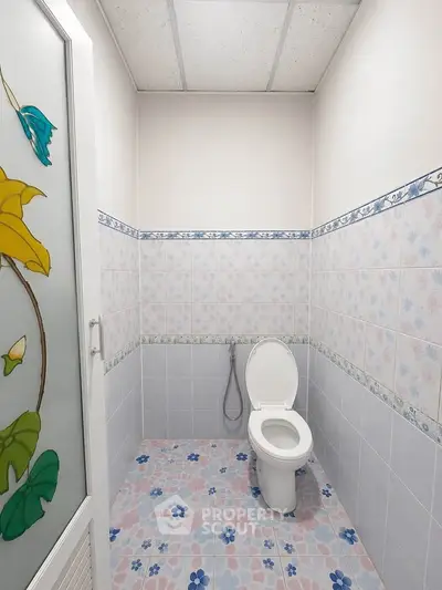 Compact bathroom with floral tiles and modern toilet in a cozy real estate property.
