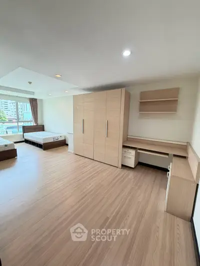 Spacious bedroom with modern wooden flooring and built-in wardrobe, featuring large windows for natural light.