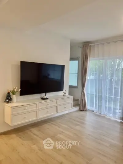 Spacious living room with modern TV setup and large window view