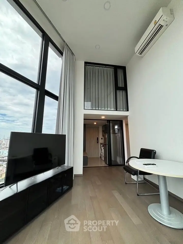 Modern loft apartment with high ceilings and large windows, featuring a sleek living area and compact kitchen.