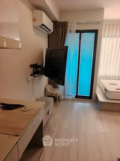 Modern bedroom with wall-mounted TV and air conditioning, featuring a minimalist design and natural light.