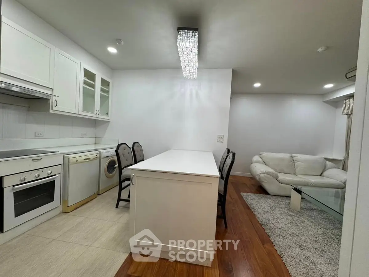 Modern open kitchen with sleek design and cozy living area, featuring a washing machine and oven.