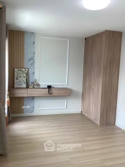 Modern bedroom with wooden flooring and built-in wardrobe, featuring elegant wall decor and natural light.