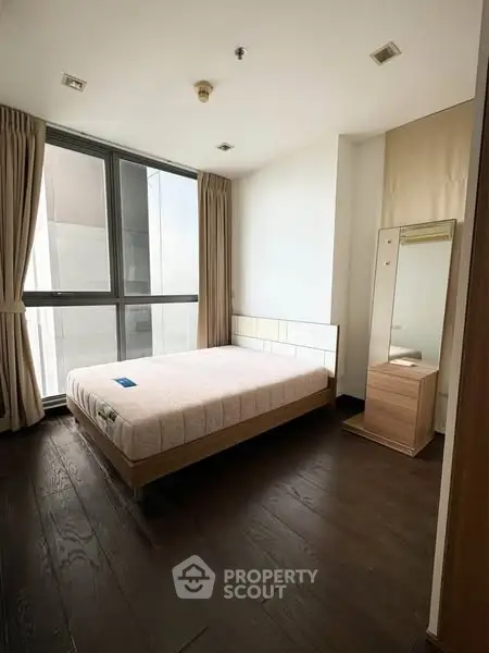 Modern bedroom with large window and wooden flooring in a stylish apartment.