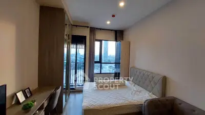Modern bedroom with city view, featuring a cozy bed, desk, and large windows for natural light.